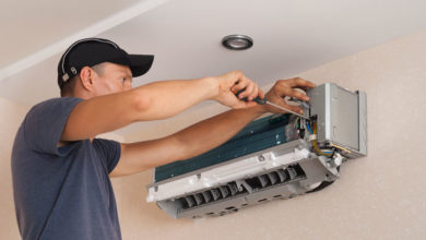 A person in a cap uses a screwdriver to repair or install a wall-mounted air conditioning unit.
