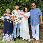 Meet Our Team: Five people, including a baby, stand outdoors in front of green bushes, posing for a group photo.