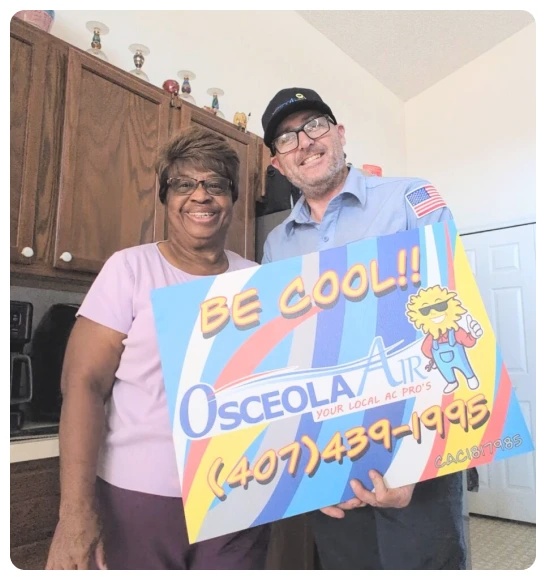 A smiling woman and a man in a work uniform hold a colorful Osceola Air sign with the text “BE COOL!!” and a phone number in a kitchen.