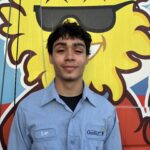 Meet Our Team: A young man in a light blue work shirt with a name tag that says "Evan" stands in front of a colorful van featuring a cartoon sun with sunglasses.