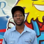 Meet Our Team: A man in a light blue Osceola uniform shirt and black cap stands in front of a colorful cartoon mural.