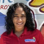 Meet Our Team: A woman with curly dark hair wearing a red Osceola Air A/C & Plumbing Pros shirt stands in front of a colorful painted van.