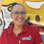 Meet Our Team: A woman wearing glasses and a red polo shirt with the "Osceola Air & Plumbing Pros" logo stands in front of a van decorated with a large sun graphic.