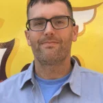 Meet Our Team: A man with short brown hair and glasses, wearing a gray work shirt with a name tag reading "Richard," stands in front of a yellow background with graphic designs.